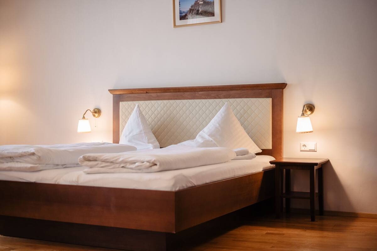 Una cama bien hecha con cabecera de madera, dos lámparas de noche y una mesita auxiliar.