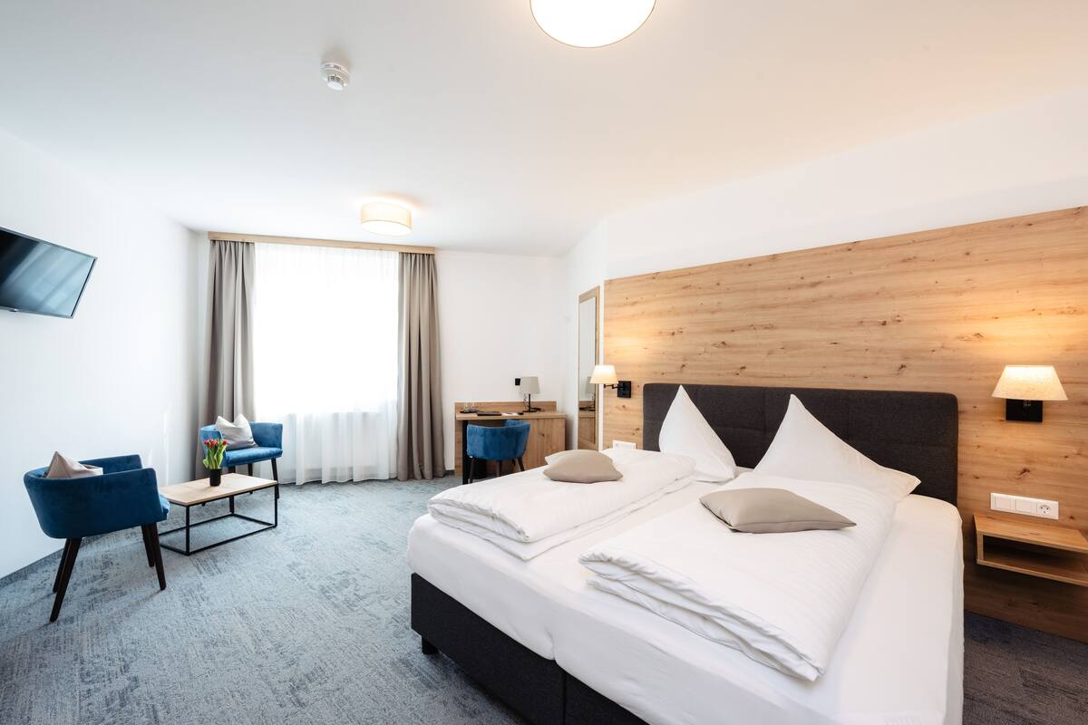 Una habitación de hotel con una cama grande, un escritorio, dos sillas azules, un televisor y un cabecero de madera.