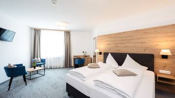 A hotel room with a large bed, a desk, two blue chairs, a TV, and a wooden headboard.