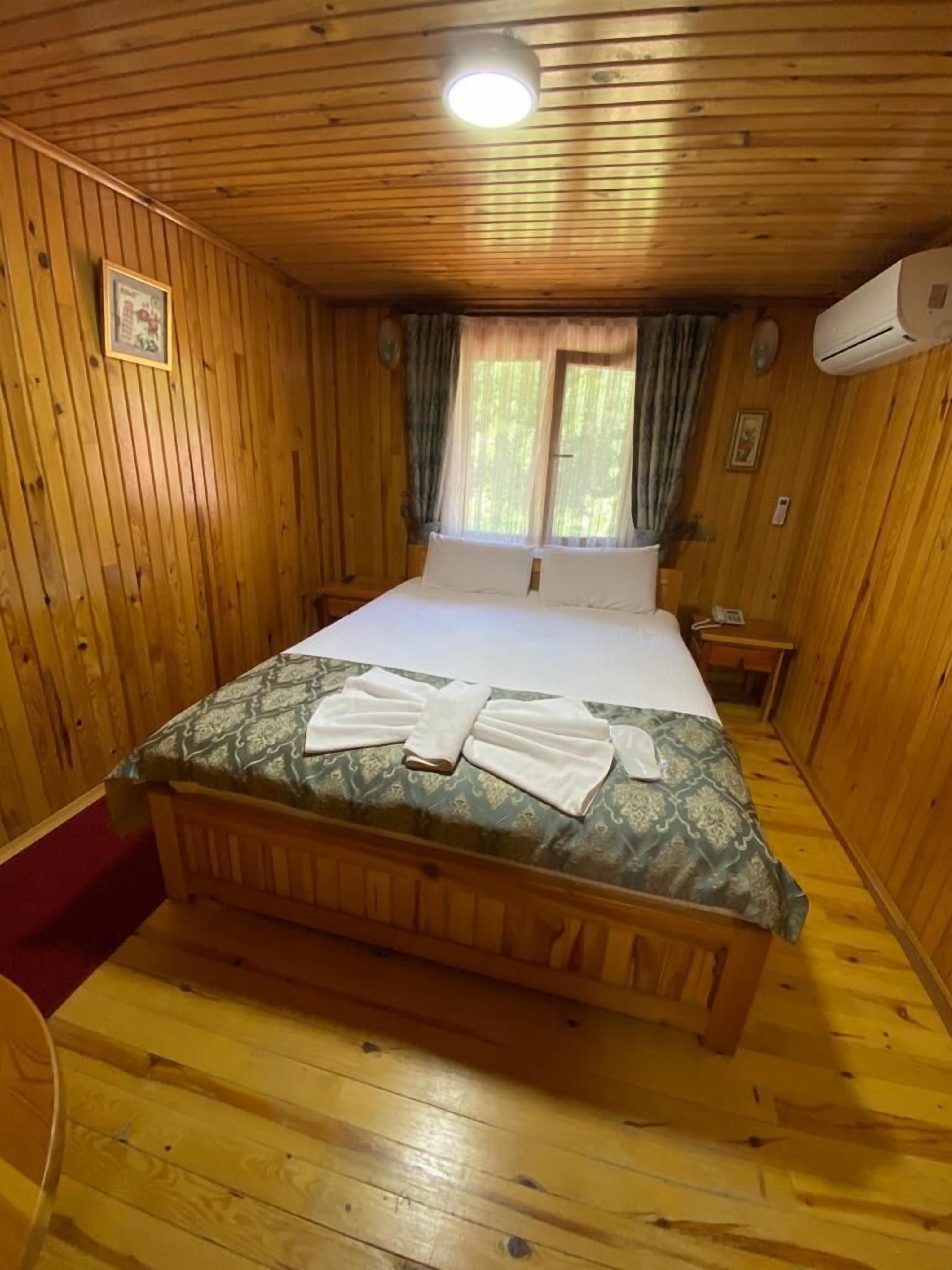 Un dormitorio de cabaña de madera con una cama, una mesita de noche, una ventana con cortinas y un equipo de aire acondicionado.