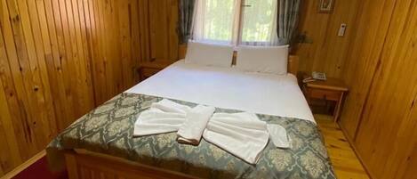 Un dormitorio de cabaña de madera con una cama, una mesita de noche, una ventana con cortinas y un equipo de aire acondicionado.