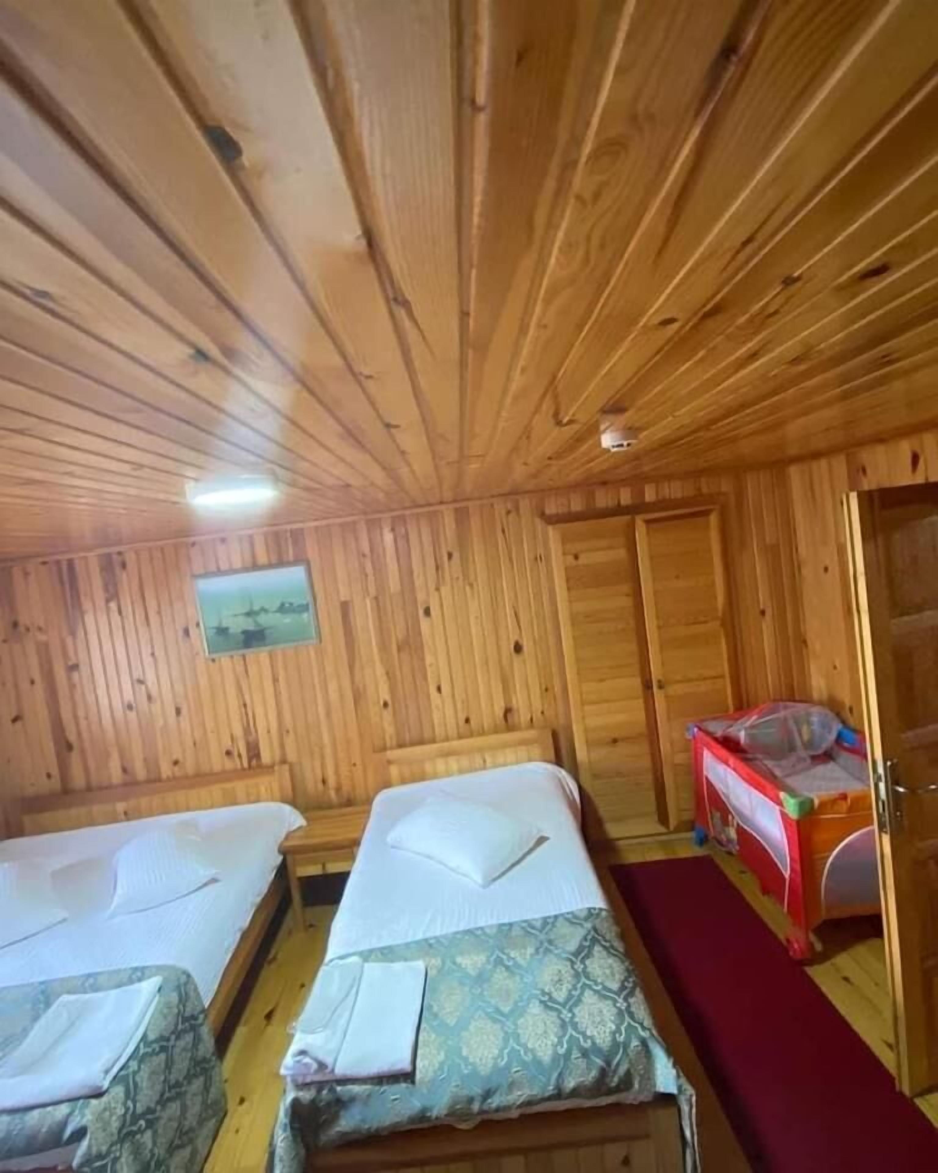 A wooden cabin room with two beds, a red carpet, and a wooden door.