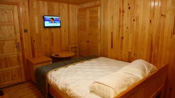 Una habitación con paneles de madera, una cama, un televisor montado en la pared y una mesita redonda.
