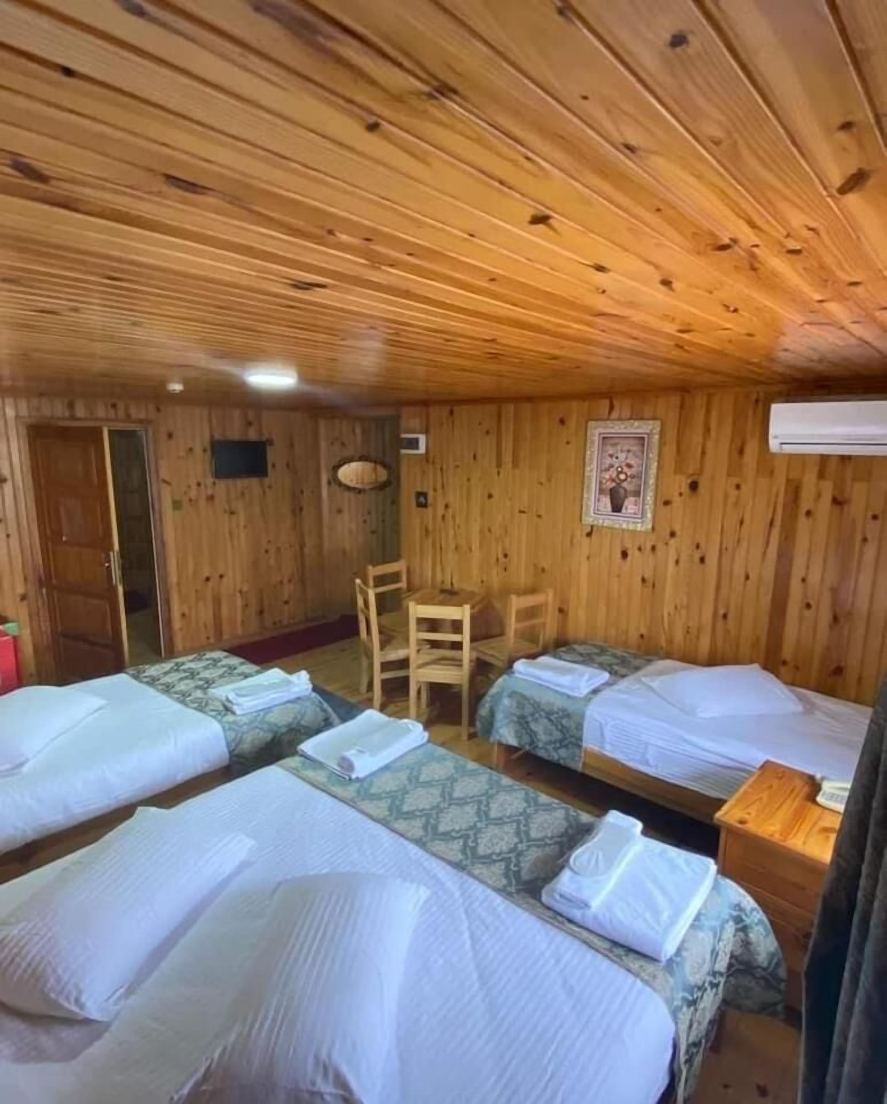 A wooden cabin room with four beds, a wooden table, and a chair.