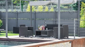 Ein Außenpoolbereich mit einer Pergola, Korbmöbeln und einem Tisch mit Flaschen und Gläsern.