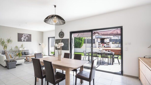 Ein modernes Wohnzimmer mit Essbereich, großen Fenstern und Blick auf die Terrasse.