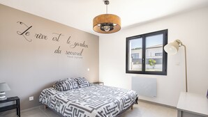 Ein Schlafzimmer mit Bett, Nachttisch, Lampe, einer Wand mit Zitat und einem Fenster mit Aussicht.