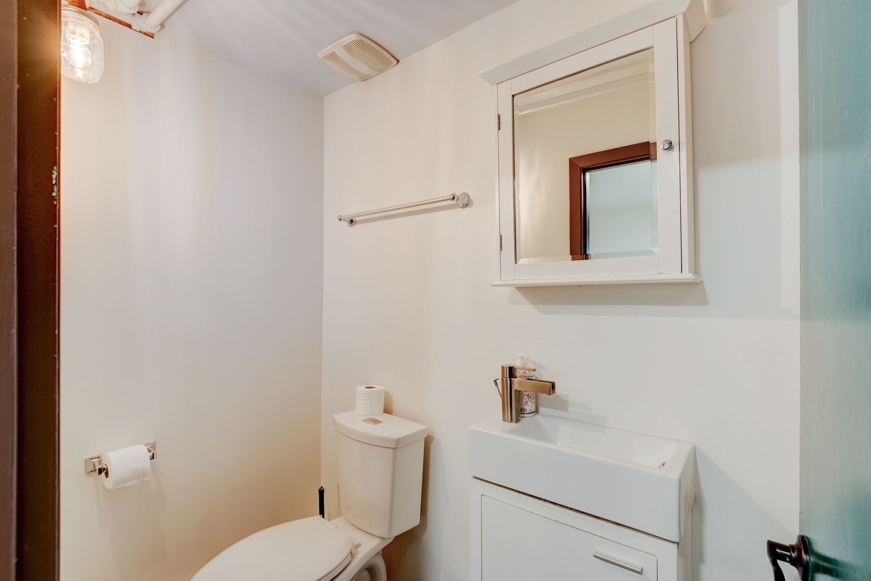 A bathroom with a toilet, a sink, a mirror, and a towel rack.