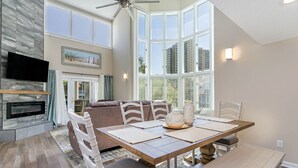 Un comedor amplio con techo alto, ventanas grandes, chimenea y televisor montado en la pared.