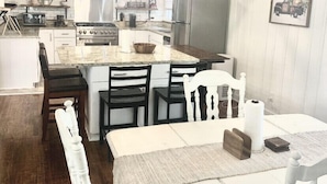 Een moderne keuken met witte kasten, een centraal eiland en een eethoek met witte stoelen en een tafel.