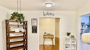 Een modern interieur met een houten bank, een bord met een welkomstboodschap en een kleine tafel met een plant.