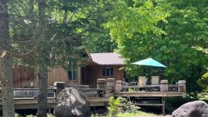 A wooden cabin with a deck, surrounded by trees and rocks. - Luxury Cabin with Indoor Heated SaltWater Pool! (Old Forge)