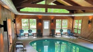 An indoor swimming pool with wooden walls and ceiling, surrounded by several chairs. - Luxury Cabin with Indoor Heated SaltWater Pool! (Old Forge)