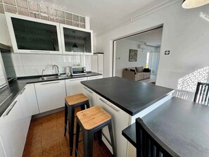 Une cuisine moderne avec des meubles blancs, un plan de travail noir et deux tabourets en bois.