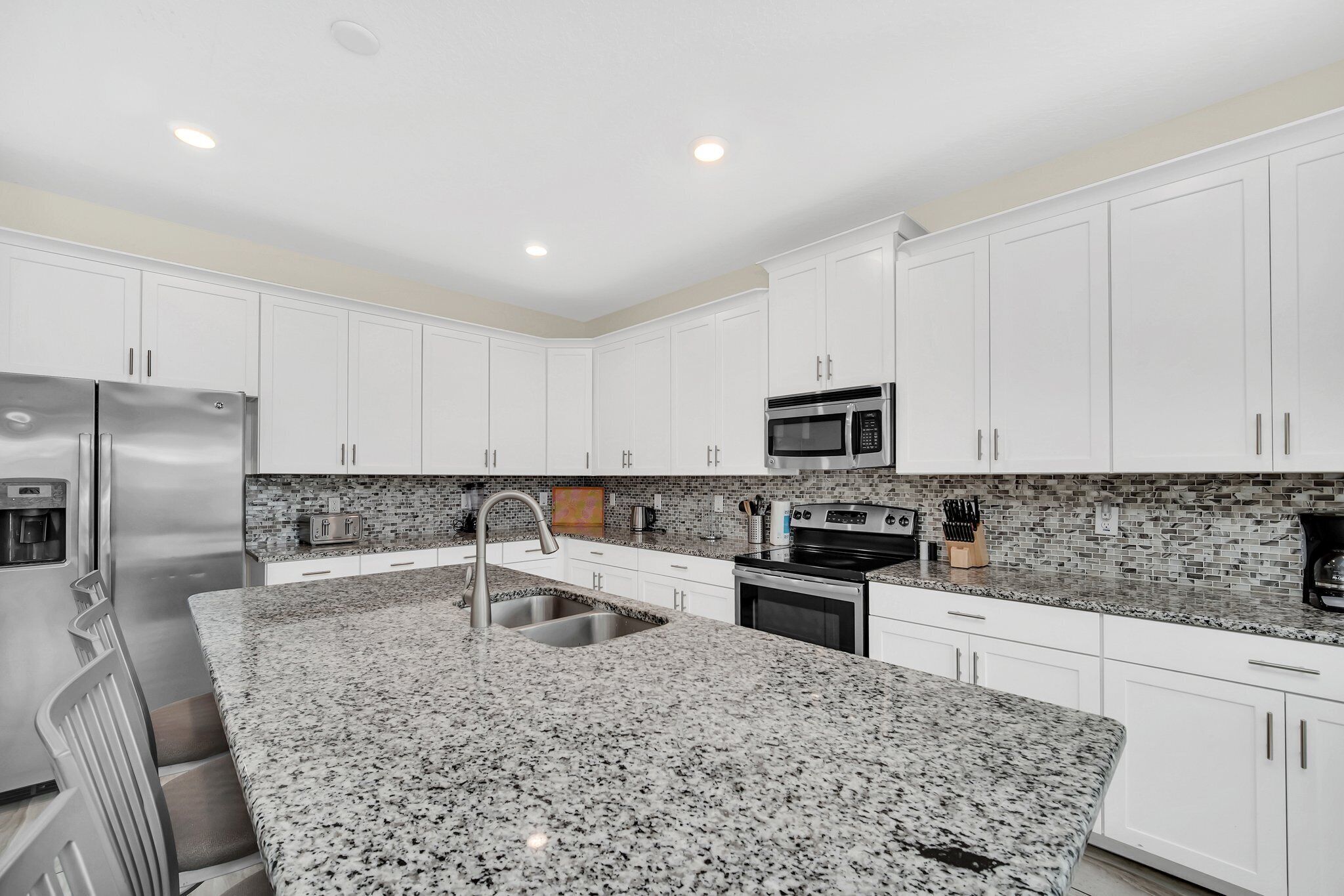Una cocina moderna con armarios blancos, encimeras de granito, electrodomésticos de acero inoxidable y un salpicadero de azulejos.