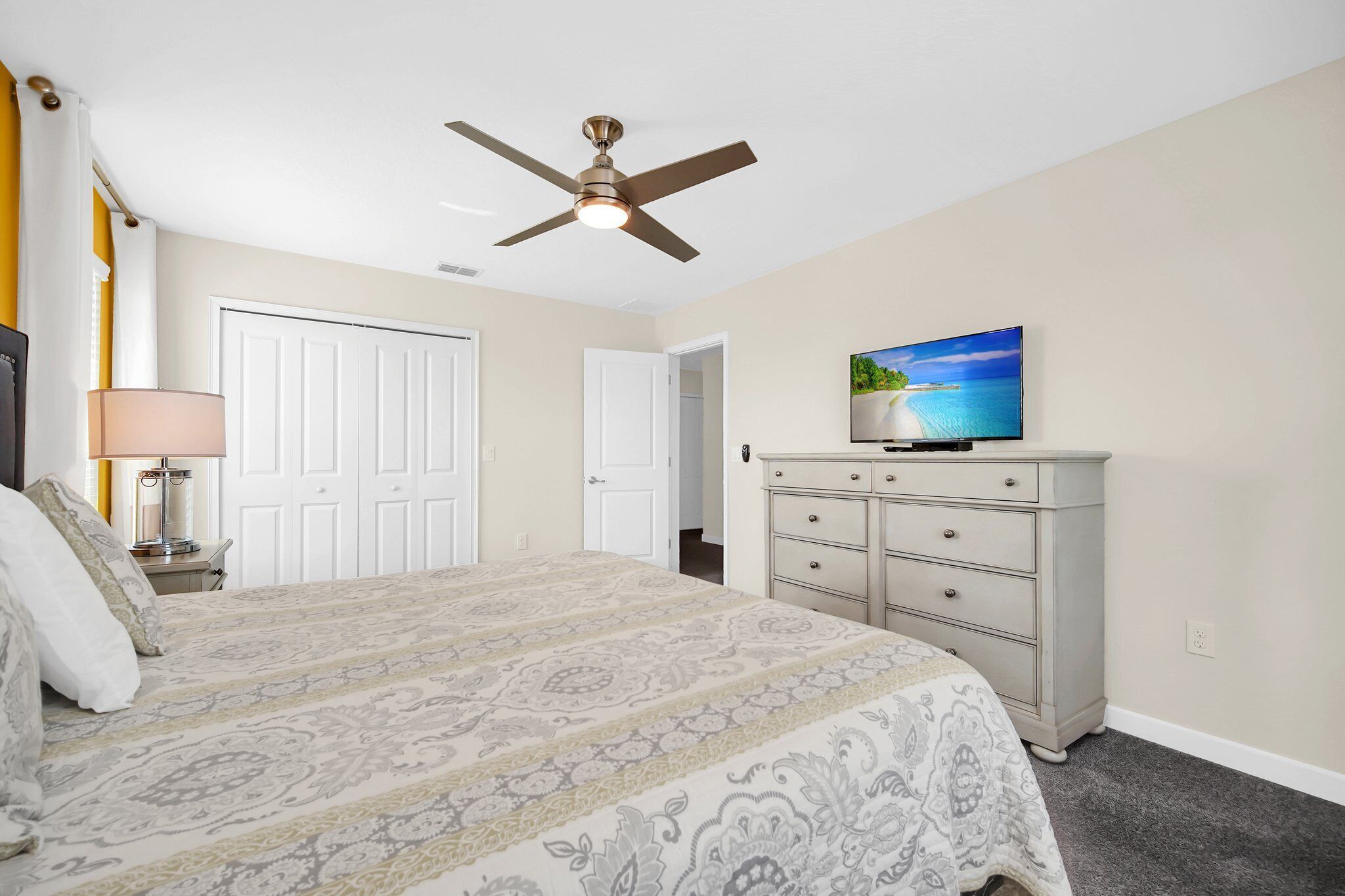 A bedroom with a bed, a ceiling fan, a dresser, a television, and a door.
