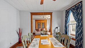 A dining room with a wooden table, chairs, and a ceiling fan. There is a window with curtains and a view of the outside. - Home on the River - stunning views and Comfy Beds (Waterford)