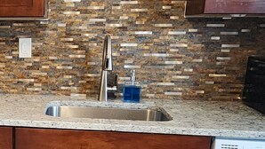 A kitchen with wooden cabinets, a granite countertop, a stainless steel sink, and a tiled backsplash. - Home on the River - stunning views and Comfy Beds (Waterford)