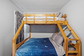 Een stapelbed met een dekbedovertrek met sterrenhemel, een houten hoofdbord en een raam met gordijnen met een patroon.