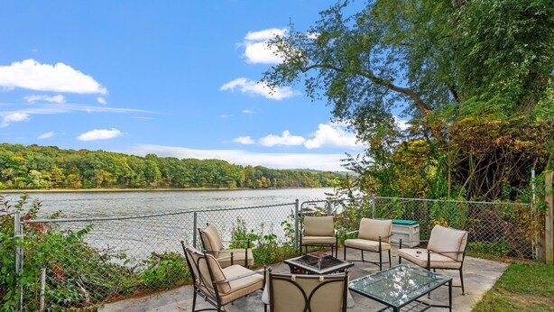 An outdoor patio with a view of a lake, surrounded by greenery and a fence. - Home on the River - stunning views and Comfy Beds (Waterford)