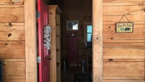 L’entrée d’un chalet en bois, avec une porte rouge, une enseigne indiquant « Escalier de secours Fernandez » et une autre qui dit « Essuyez vos pattes ».