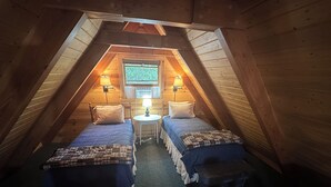Une petite chambre mansardée avec deux lits, une table et deux lampes.