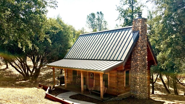 Une cabane rustique avec un toit en métal incliné, une cheminée en pierre et une véranda en bois.