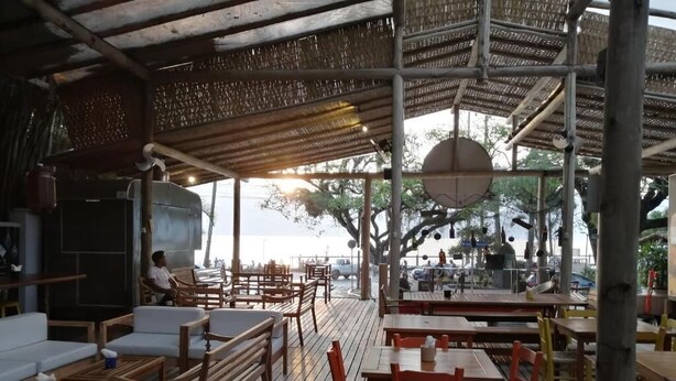 Un restaurant en plein air avec des tables et des chaises en bois, un espace de restauration couvert et une vue sur la mer.