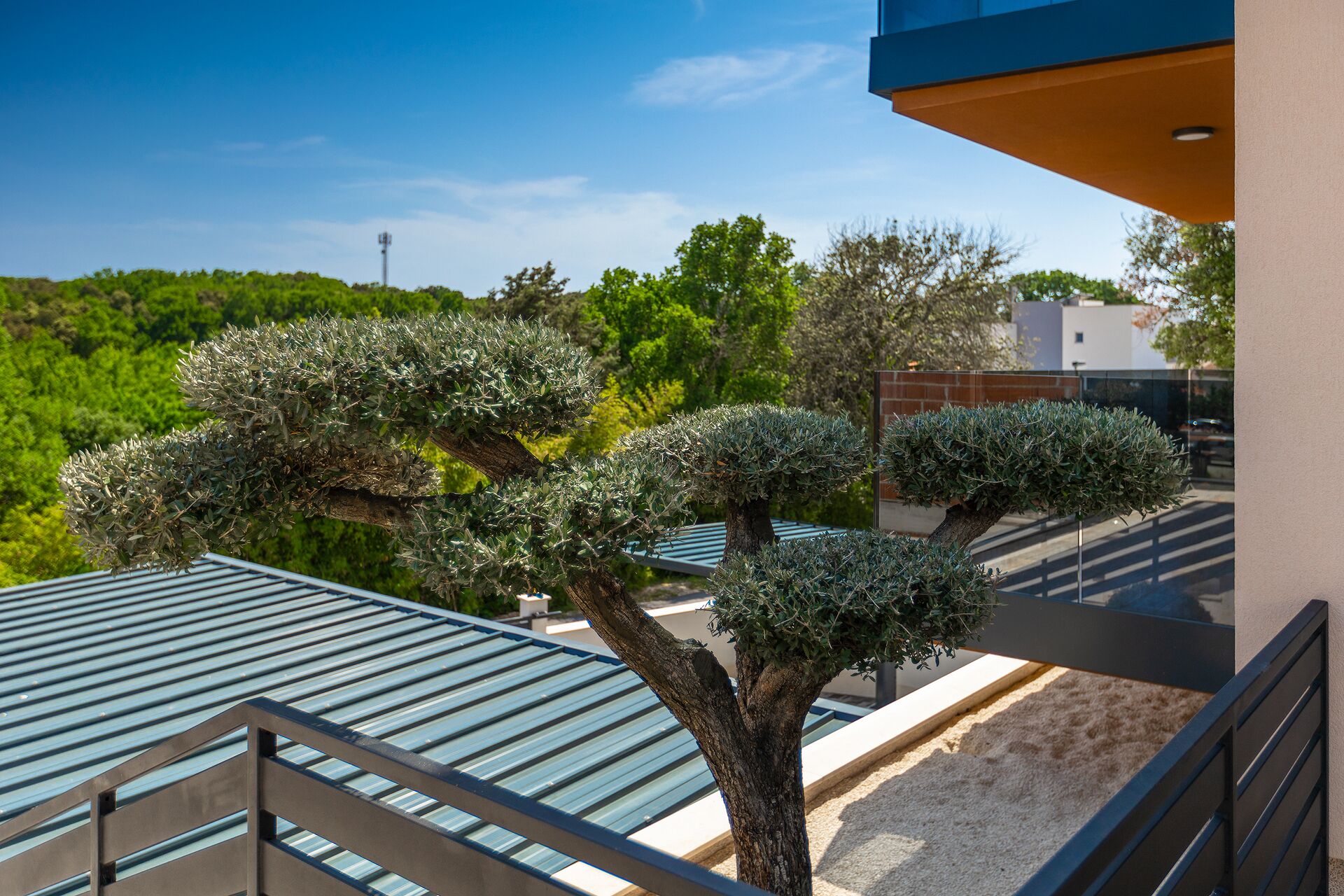 Ein Balkon mit Blick auf einen gepflegten Garten, ein modernes Gebäude und einen strahlend blauen Himmel.
