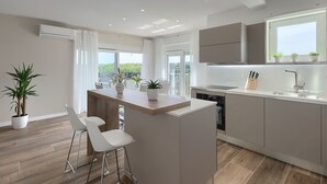 A modern kitchen with a central island, bar stools, and a view of greenery outside.