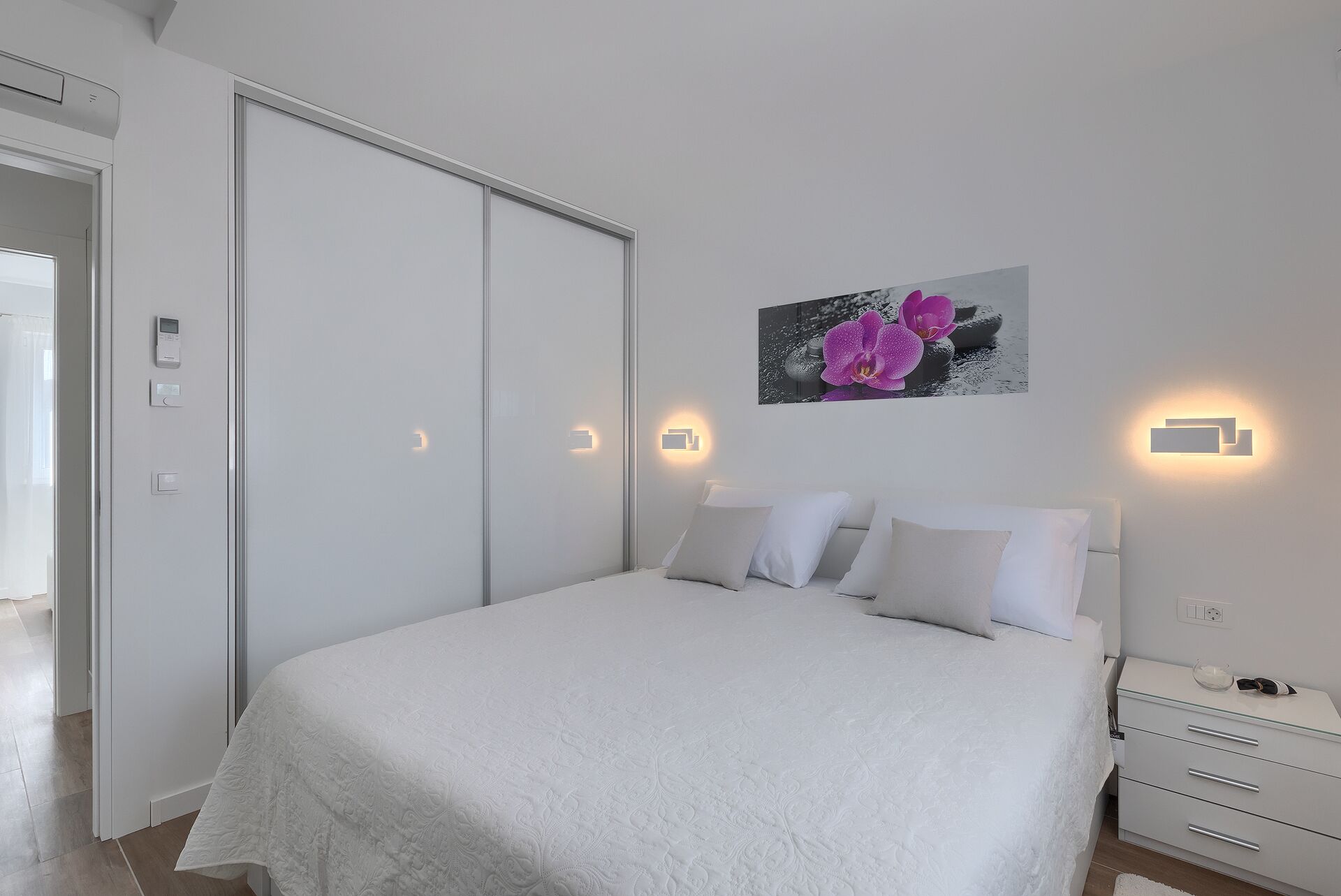 A bedroom with a bed, bedside tables, a wardrobe, and a wall-mounted light fixture.