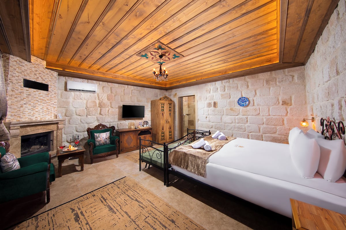 Una habitación acogedora con pared de piedra, chimenea, cama y sillón verde.