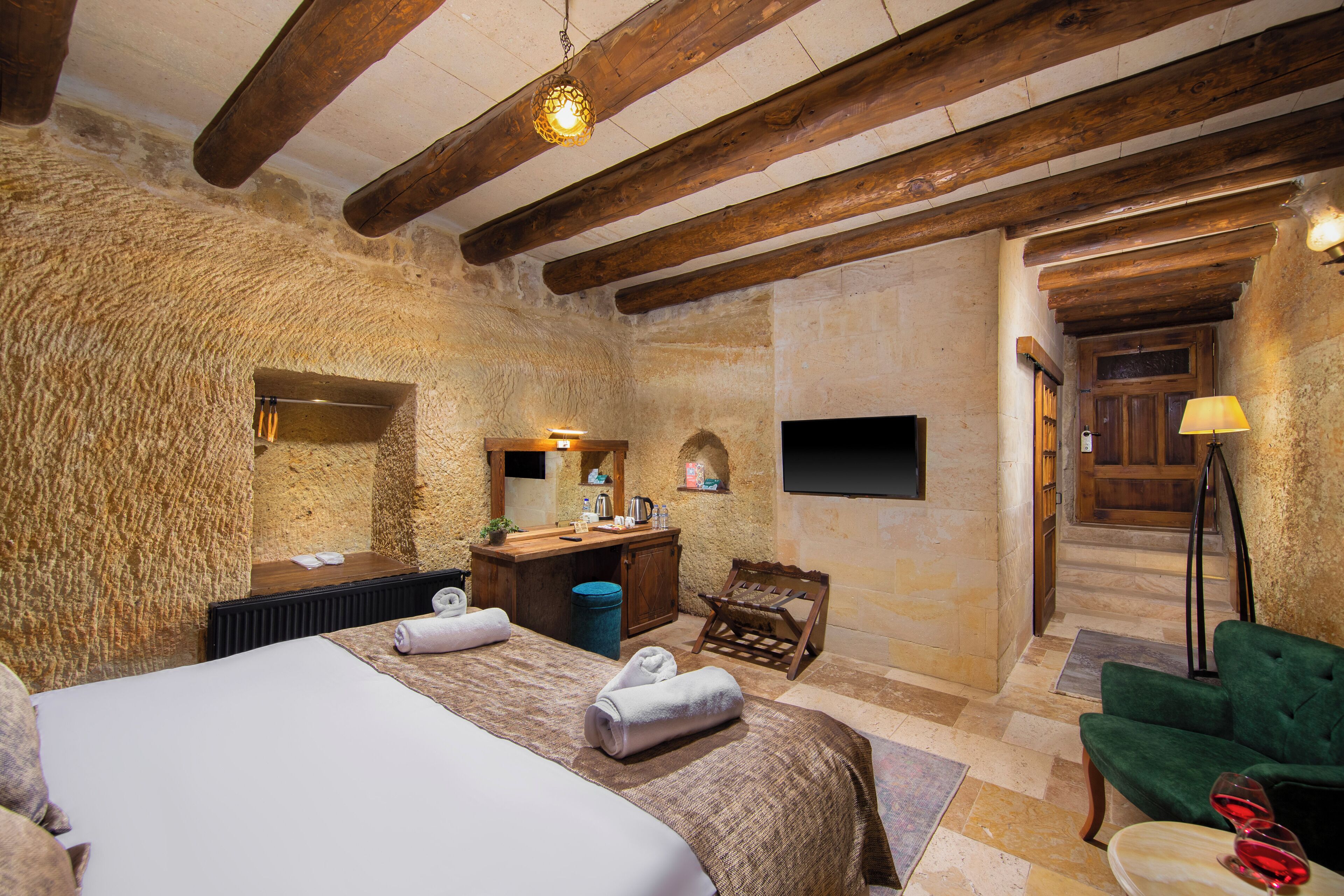 Una habitación rústica con una cama grande, vigas de madera, paredes de piedra, un escritorio de madera, una silla y un sofá verde.