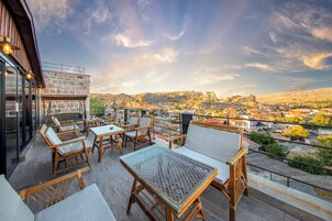 Un espacio al aire libre con mobiliario de mimbre y una mesa de vidrio, con vistas a un pueblo con una colina y un castillo destacados.