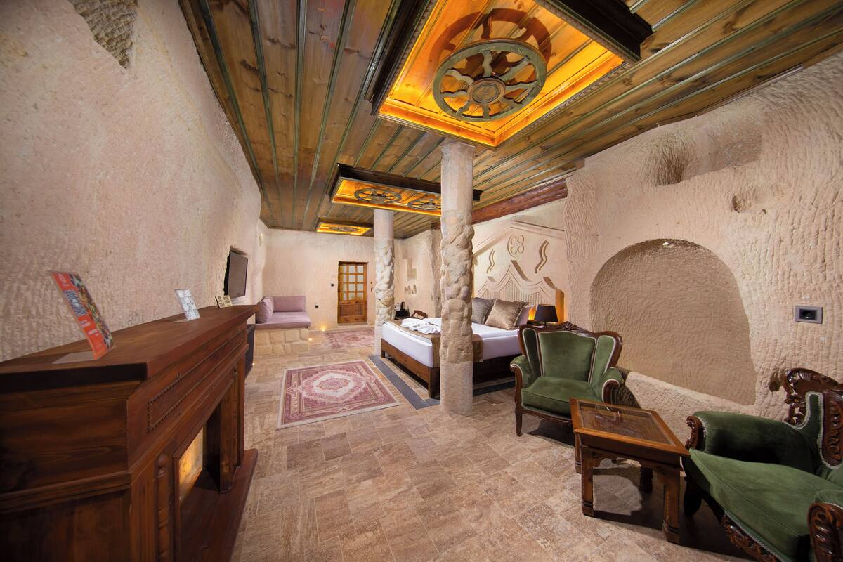 Una habitación con cama, un escritorio de madera, un sillón verde y una pared de piedra.