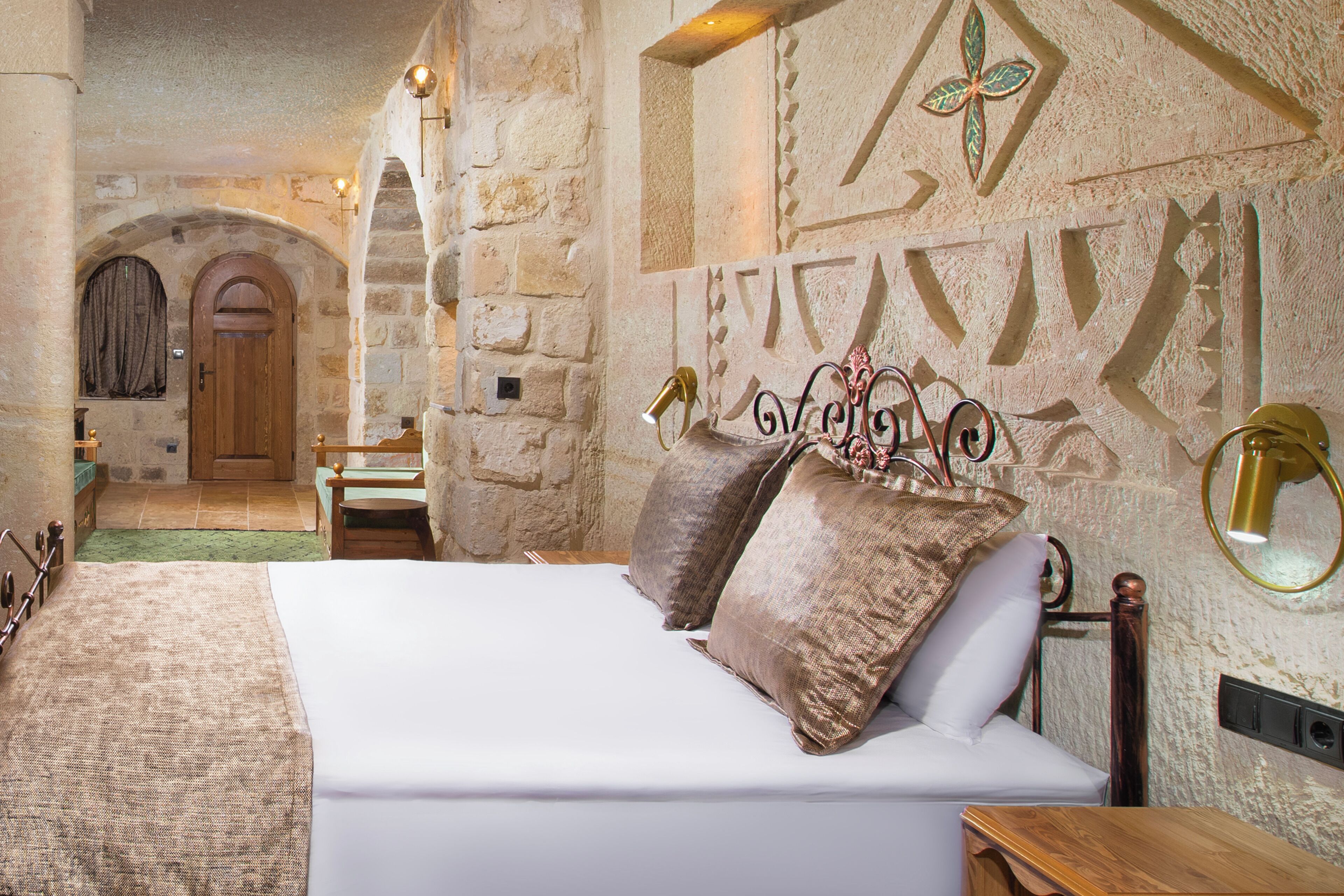 A bedroom with a stone wall, a wooden door, and a bed with pillows.