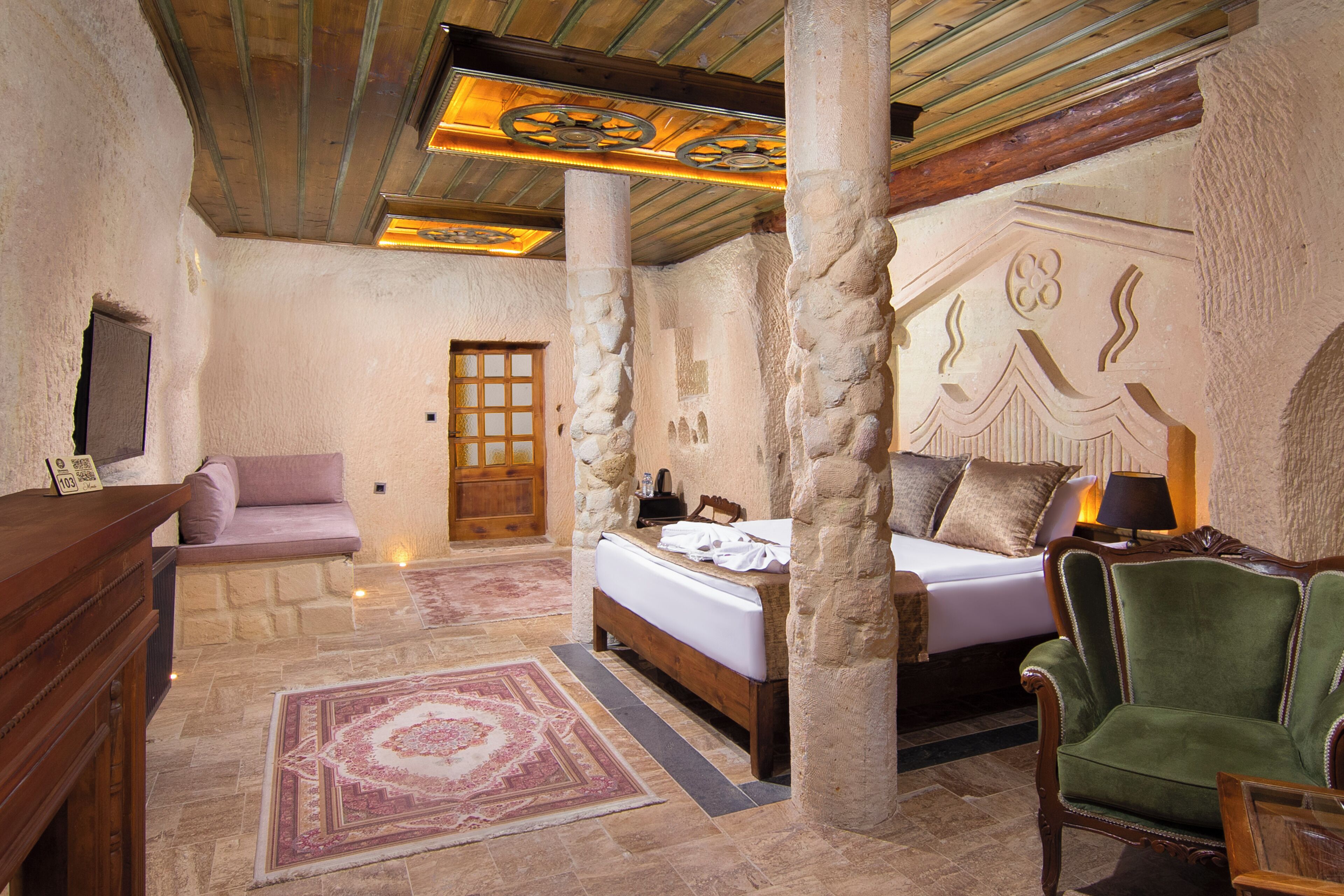 A room with a bed, a chair, a desk, and a stone pillar.