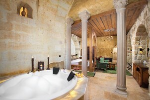 Un baño con paredes de piedra, una bañera grande, vigas de madera y un sofá verde al fondo.
