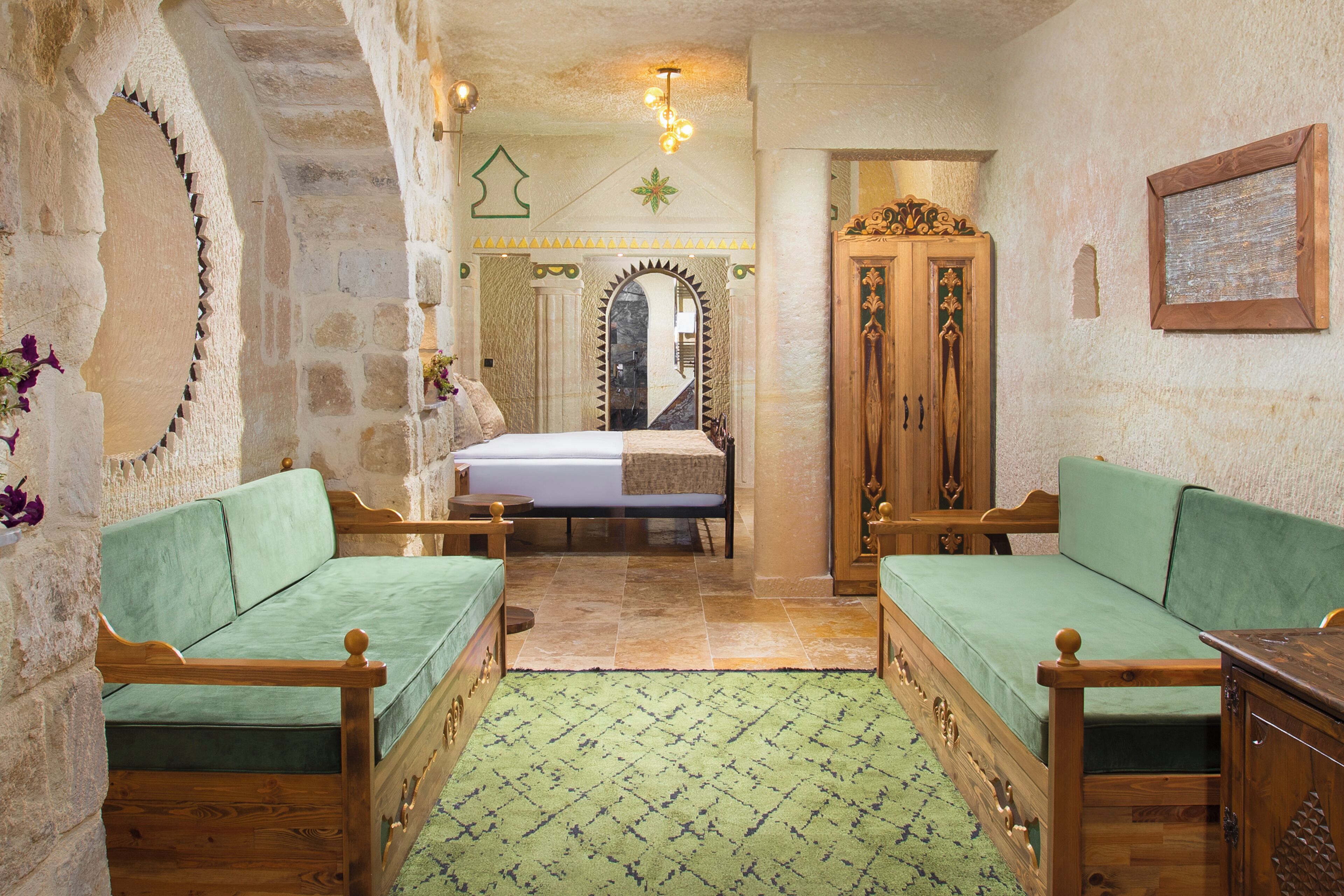 A room with a bed, two wooden chairs, a wooden cabinet, and a mirror.