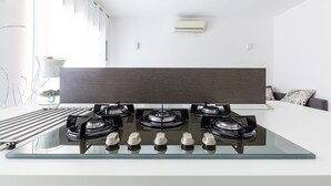 A modern kitchen with a glass-top stove, a dark wood panel above the stove, and a white countertop. - MIA - Modern Flat Close Airport and Center (Napoli)