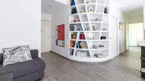A modern living room with a grey sofa, a white curved bookshelf, and a red door in the background. - MIA - Modern Flat Close Airport and Center (Napoli)