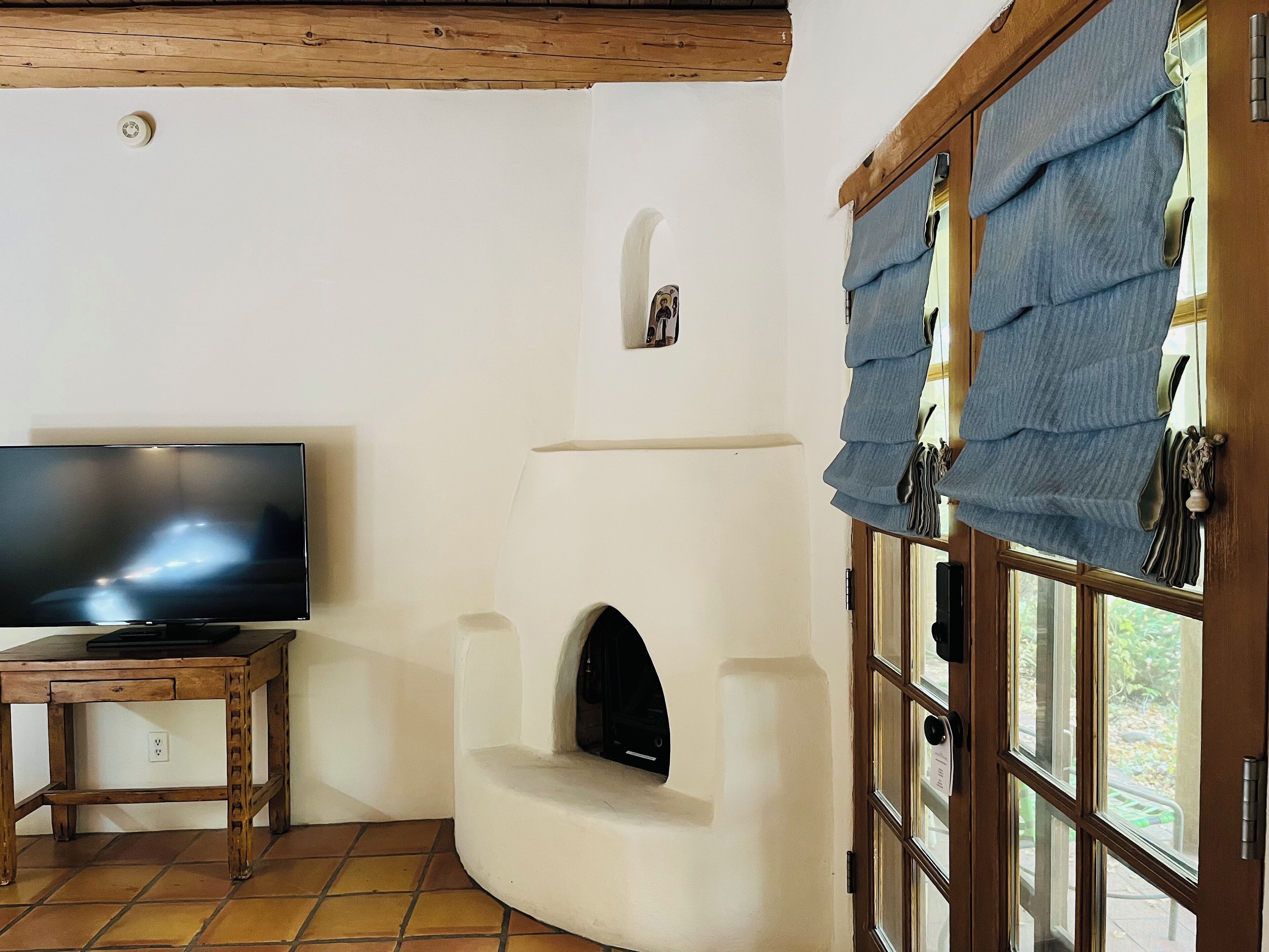 Una sala de estar con una televisión sobre una mesa de madera, una chimenea y una ventana con cortinas.