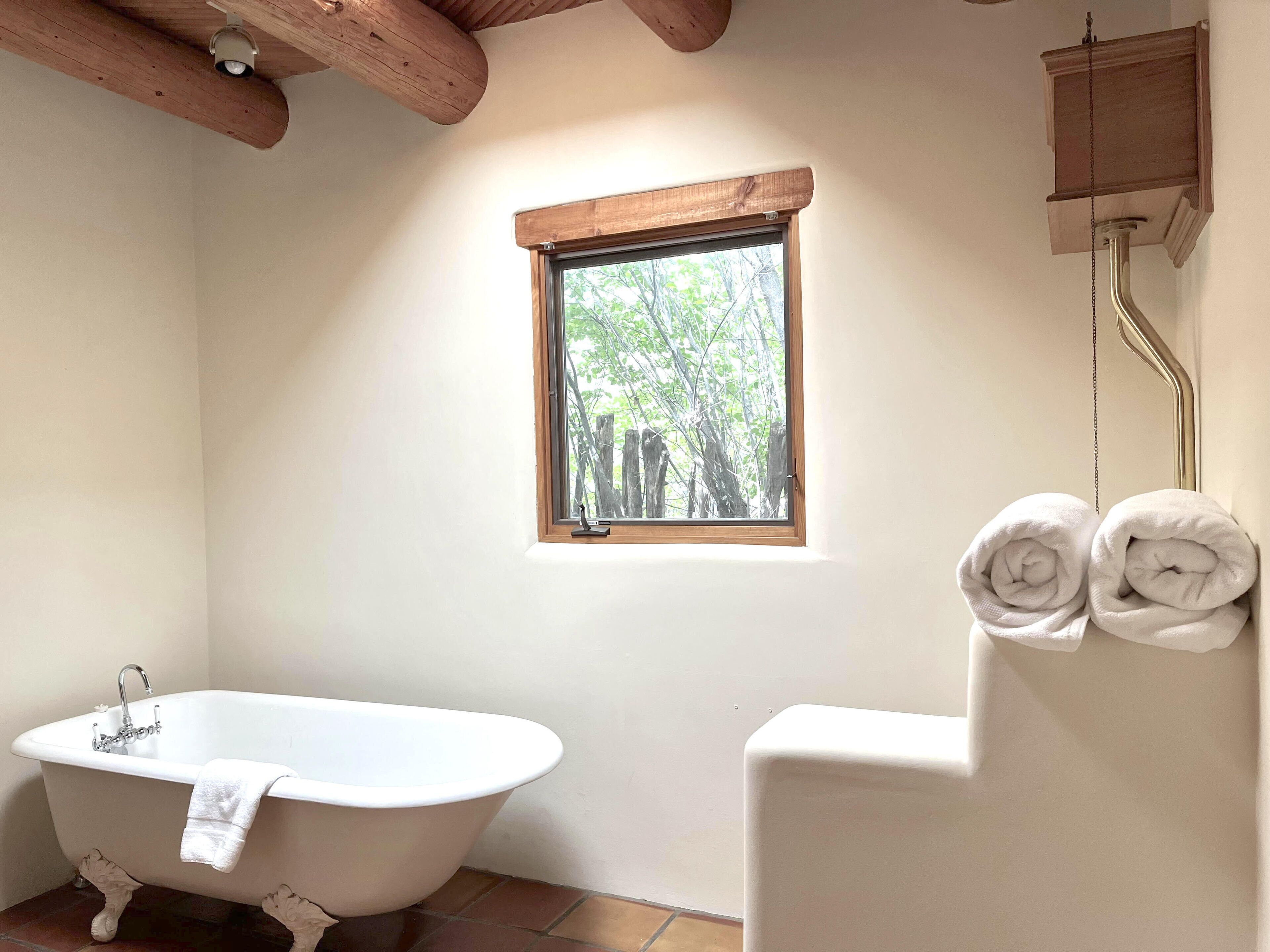 Une salle de bain avec une baignoire sur pieds, une fenêtre donnant sur les arbres et un porte-serviettes avec deux serviettes.