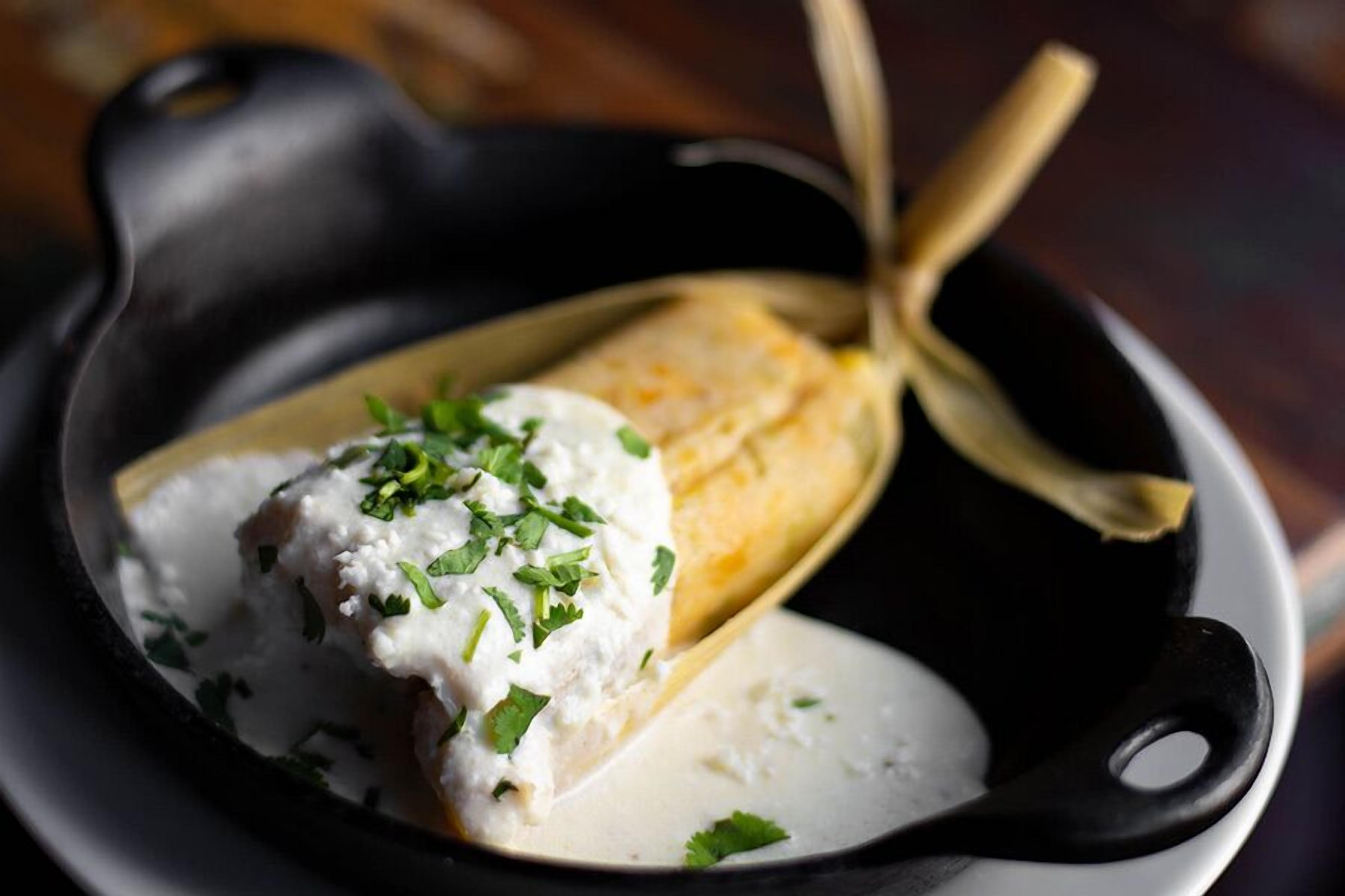 A skillet with a piece of corn on the cob topped with a creamy sauce and garnished with herbs.