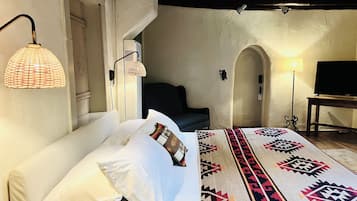 Une chambre à coucher avec un lit, des oreillers, un tapis à motifs, un téléviseur et des lampes fixées au mur.