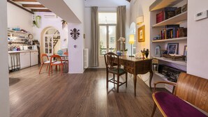 A cozy interior with a wooden dining table, chairs, a bookshelf, and a kitchen area with cabinets and a hanging plant. - Florence Hideaway by Mmega (Florence)