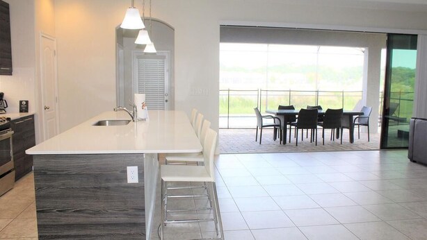 A modern kitchen with a large island, a dining area with chairs, and a view through large windows. - Stunning Lake View Balmoral Estate 4 Bedroom (Haines City)