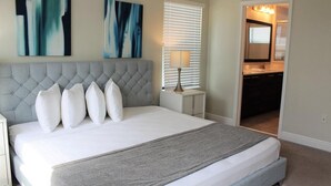A bedroom with a tufted headboard, a large bed with white bedding, a bedside table with a lamp, and abstract art on the wall. - Stunning Lake View Balmoral Estate 4 Bedroom (Haines City)