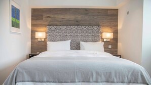 A neatly made bed with a grey and white patterned bedspread, two white pillows, and a wooden headboard with a floral design. - Stunning Rare Soho Gem (London)