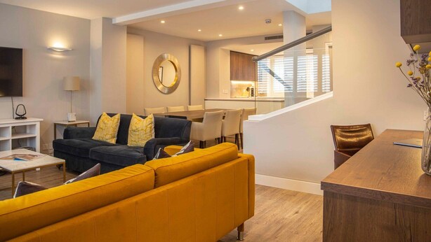 A modern living room with a sofa, a coffee table, and a TV. There is a staircase leading to a dining area. - Stunning Rare Soho Gem (London)